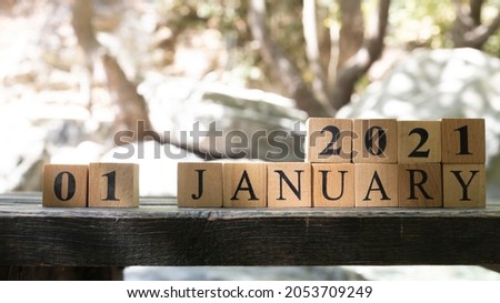 January was created from wooden cubes. Outdoors on table, trees in background. Close up.