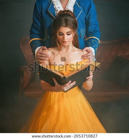 Woman princess holding a book without title cover design reads the text. Fantasy man enchanted prince hugging a beautiful lady by shoulders. Girl in yellow medieval historical dress vintage gown Royalty-Free Stock Photo #2053710827
