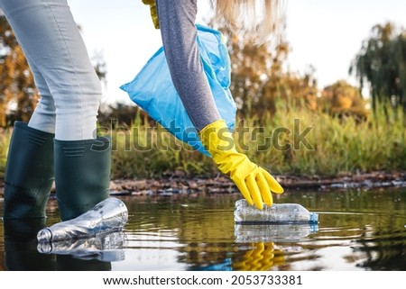 Environmental cleanup. Volunteer picking up plastic bottle from polluted river or lake. Water pollution with plastic garbage Royalty-Free Stock Photo #2053733381