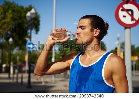 Fit young sportsman drinking water from a bottle while standing alone outdoors during the day