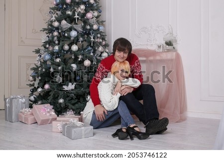young couple sitting on the living room floor next to a nicely decorated Christmas tree
