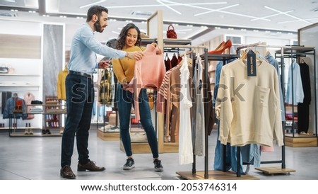 Young Female Customer Shopping in Clothing Store, Retail Sales Associate Helps with Advice. Diverse People in Fashionable Shop, Choosing Stylish Clothes, Colorful Brand with Sustainable Designs Royalty-Free Stock Photo #2053746314