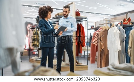 Clothing Store: Businesswoman Uses Tablet Computer, Talks to Visual Merchandising Specialist, Collaborate To Create Stylish Collection. Small Business Fashion Shop Sales Manager Talks to Designer. Royalty-Free Stock Photo #2053746320