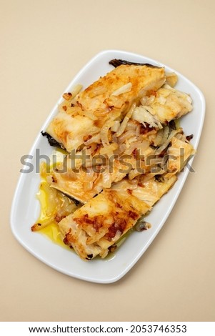 fried cod fish with onion and olive oil on white dish on brown background