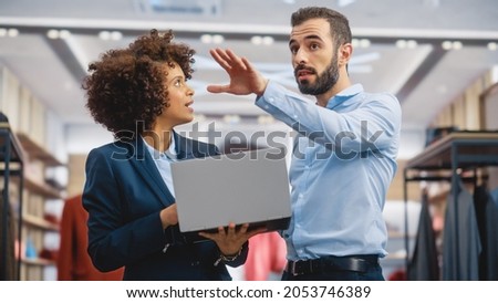 Clothing Store: Businesswoman Uses Laptop Computer, Talks to Visual Merchandising Specialist, Collaborate To Create Stylish Collection. Small Business Fashion Shop Sales Manager Talks to Designer. Royalty-Free Stock Photo #2053746389