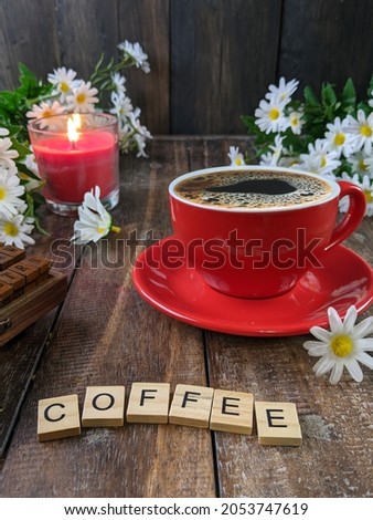 still life photo of a cup of coffee in a red cup on a wooden table with red candle and flowers