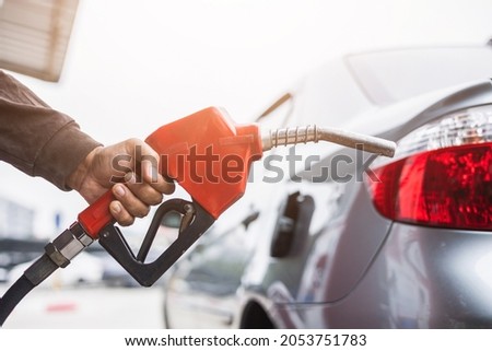 A gas station worker holds a fuel dispenser to fill the car with fuel. A young man's hand holds a gas nozzle to refuel with self-service in a gas station. Royalty-Free Stock Photo #2053751783