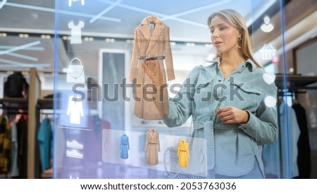 Beautiful Female Customer Using 3D Augmented Reality Digital Interface in Modern Shopping Center. Shopper is Choosing Fashionable Bags, Stylish Garments in Clothing Store. Futuristic VFX UI Concept. Royalty-Free Stock Photo #2053763036