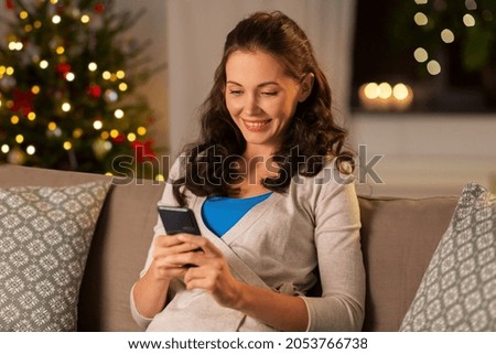 winter holidays, technology and people concept - smiling woman with smartphone at home over christmas tree lights on background