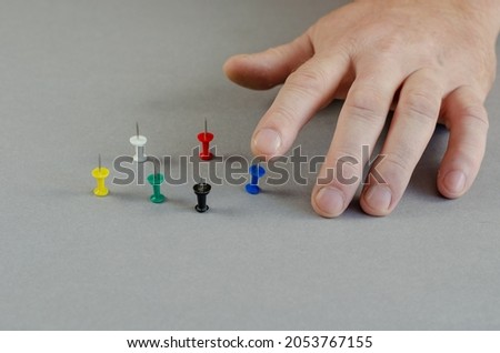 One Hand and push pins on gray background. Man presses one sharp thumbtack with an index finger. Close-up. Selective focus. Royalty-Free Stock Photo #2053767155