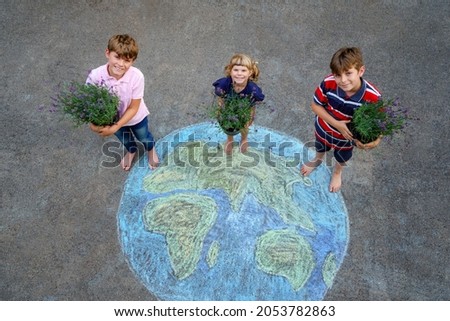 Little preschool girl and two school kids boys with flowers on earth globe painting with colorful chalks on ground. Happy earth day concept. Creation of children for saving world, environment ecology.