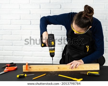 A young girl works with a drill. Working environment in a carpentry workshop. Cordless cordless drill - screwdriver with drill. Construction tools set. Professional repair equipment. Royalty-Free Stock Photo #2053798784