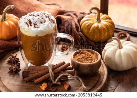 Pumpkin spice latte with cinnamon sticks on a wooden platter and pumpkins by a window