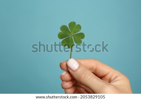 Woman holding green four leaf clover on light blue background, closeup Royalty-Free Stock Photo #2053829105