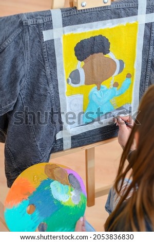 Artist with color palette drawing on a jacket. Girl with a brush creating individual clothes. View from behind of artist
