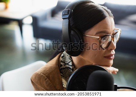 asian radio host in glasses and headphones looking away during broadcast