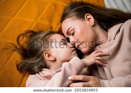 beautiful mom and daughter are lying on a blanket on the bed and kissing