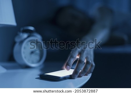 Woman sleeping in her bed and receiving a phone call late at night, she is checking her smartphone Royalty-Free Stock Photo #2053872887