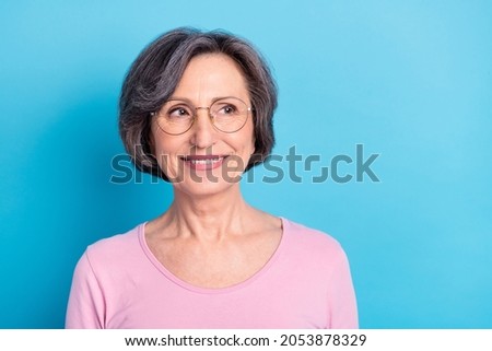 Photo of mature smiling positive dreamy woman in glasses look copyspace dreaming isolated on blue color background