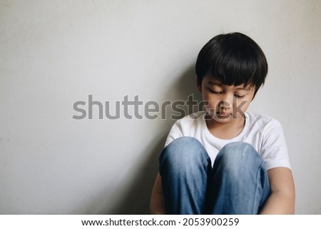 Little Asian boy sitting in the corner of the house feeling sad from family problems Royalty-Free Stock Photo #2053900259