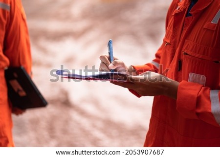 Action of safety officer is writing and check on checklist document during safety audit and inspection at drilling site operation. Industrial expertise occupation photo. Royalty-Free Stock Photo #2053907687