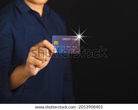 Midsection of a businessman in a blue shirt holding a mockup blue credit card while standing with a black background in the studio. Close-up photo. Space for text. Money and business concept.