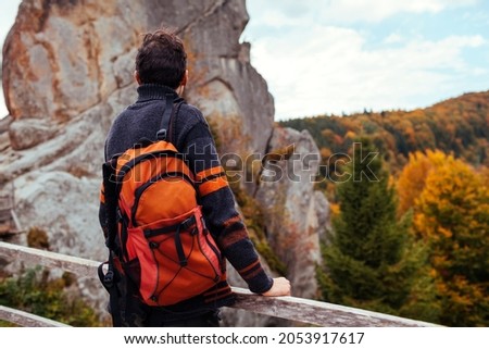 Man traveler with backpack stands by rocks in Tustan in autumn Carpathian mountains. Tourism in fall Ukraine. Hiking and recreation