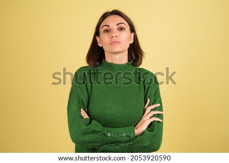 Young woman in green warm sweater serious focused unhappy look to camera with arms crossed
