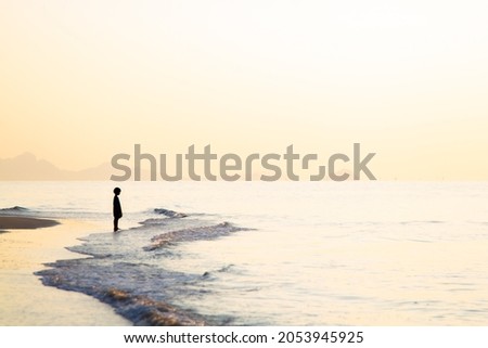 Silhouette of a lonely boy standing at the beach looking at the sea. Royalty-Free Stock Photo #2053945925