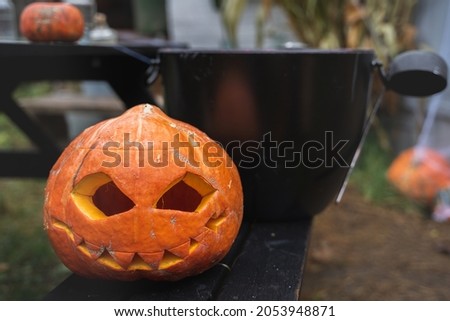 Orange pumpkin for halloween in black witch, wizard hat, jack-o-lantern with scary carved eyes, mouth.Candles on wooden table near barn. DIY home,street decoration, entertainment for children, horror.
