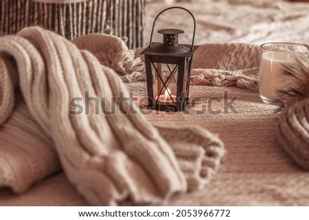 Knitted sweater, lantern with candle on beige knitted blanket. Comfort and care, cozy home concept Royalty-Free Stock Photo #2053966772
