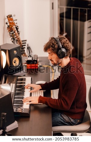 Young music producer wearing headphones recording music with electric piano at home music studio
