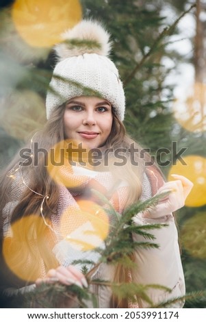 Portrait of a young beautiful girl in a hat among winter Christmas trees with lights. A park with Christmas trees on the background. Christmas mood. Tinting.
