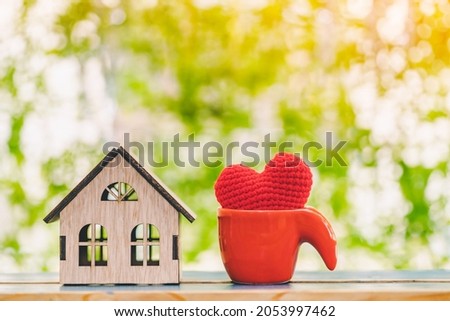 Wooden house model and red heart put in the cup on the wood on sunlight in the public park, The buying a new real estate as a gift to family or the one loved concept.