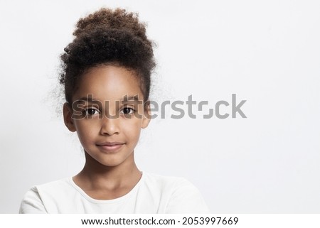 Portrait of a beautiful mixed race kid on white studio background. Beautiful young girl with afro hair. Child looks to the camera. Concept of childhood, cute schoolgirl 9-10 years old. Copy space.  Royalty-Free Stock Photo #2053997669