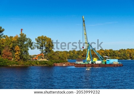 Start of construction of a bridge across the river to the island. Engineering work on a pond with a crane