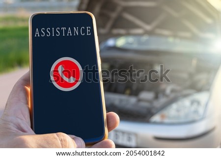 Close-up with selective focus of a phone ready to call the roadside assistance service, with a damaged car in the background. Royalty-Free Stock Photo #2054001842