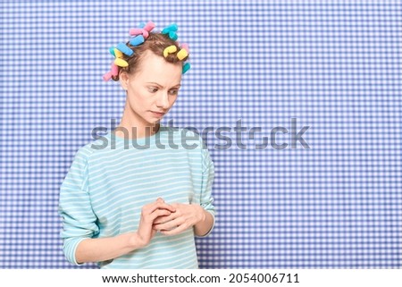 Portrait of thoughtful young woman without makeup with colorful hair curlers on head, looking melancholic and dreamy, standing over shower curtain background, with place for your text and design Royalty-Free Stock Photo #2054006711