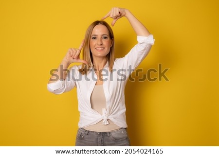 Happy woman making frame with fingers isolated on a yellow background
