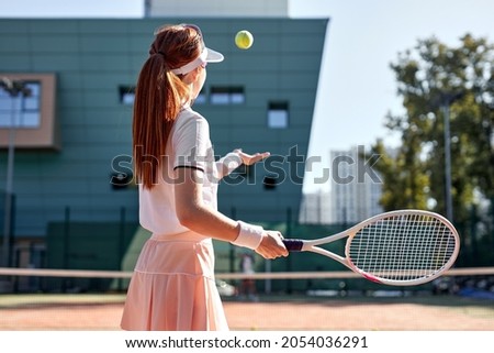 portrait of sporty lady tennis player with racket, raising throwing ball up. confident slim fit female tennis player in uniform training exercising at summer day. sport, fitness, people concept