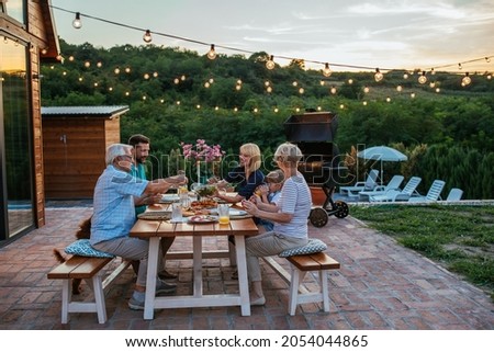 Happy family eating together outdoors. Smiling generation family sitting at dining table during dinner. Happy cheerful family enjoying meal together in garden. Royalty-Free Stock Photo #2054044865