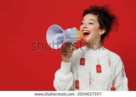 Young smiling female costumer woman 20s wear white knitted sweater with tags sale in store showroom hold scream in megaphone announces discounts sale Hurry up isolated on plain red background studio