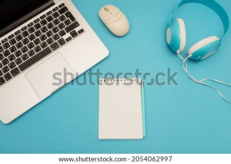 Top view of office desk with gray laptop, notepad, pen, headphones on blue background, creative designer concept, business, online learning or job concept.