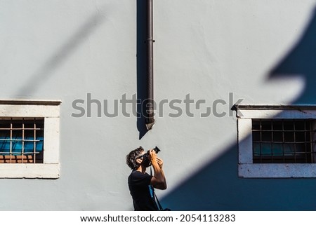 A young amateur photographer takes shots of architectural motifs on a sunny day in a minimalist setting with a simple background.