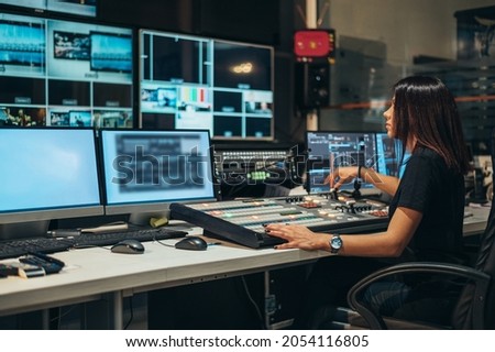 Young beautiful woman working in a broadcast control room on a tv station Royalty-Free Stock Photo #2054116805