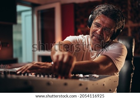 Senior hispanic music producer working on a mixing soundboard while in his studio Royalty-Free Stock Photo #2054116925