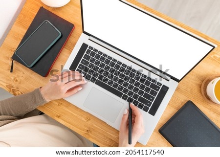 Caucasian woman sitting at the wooden table and working at the laptop. Female is laying hands on notebook and reading on blank screen. Freelancer working from home office. Top view, flat lay.