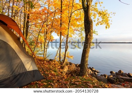 Tent beside calm lake in autumn with beautiful colorful leaves