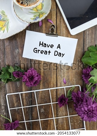 A cup of coffee, flowers and white notepad with text HAVE A GREAT DAY wish on wooden table, flat lay. Space for text