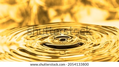 A complex pattern of concentric ripples created by a droplet of oil falling onto the surface of a viscous liquid under the effects of golden lighting and set against a blurred background for effect. Royalty-Free Stock Photo #2054133800